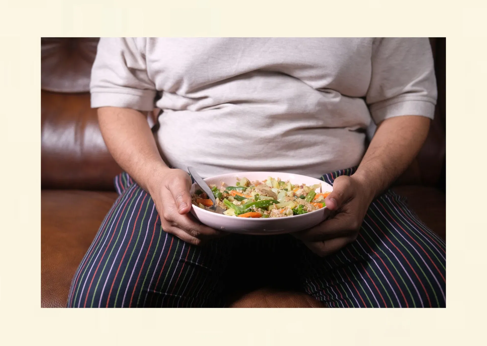 Person mit Übergewicht sitzt vor einem Teller mit gesunder Ernährung – symbolische Darstellung des Konflikts zwischen Diät und stressbedingtem Essverhalten.