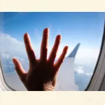 Hand einer Person vor einem Flugzeugfenster – mögliche Erfahrungen und Ursachen von Flugangst