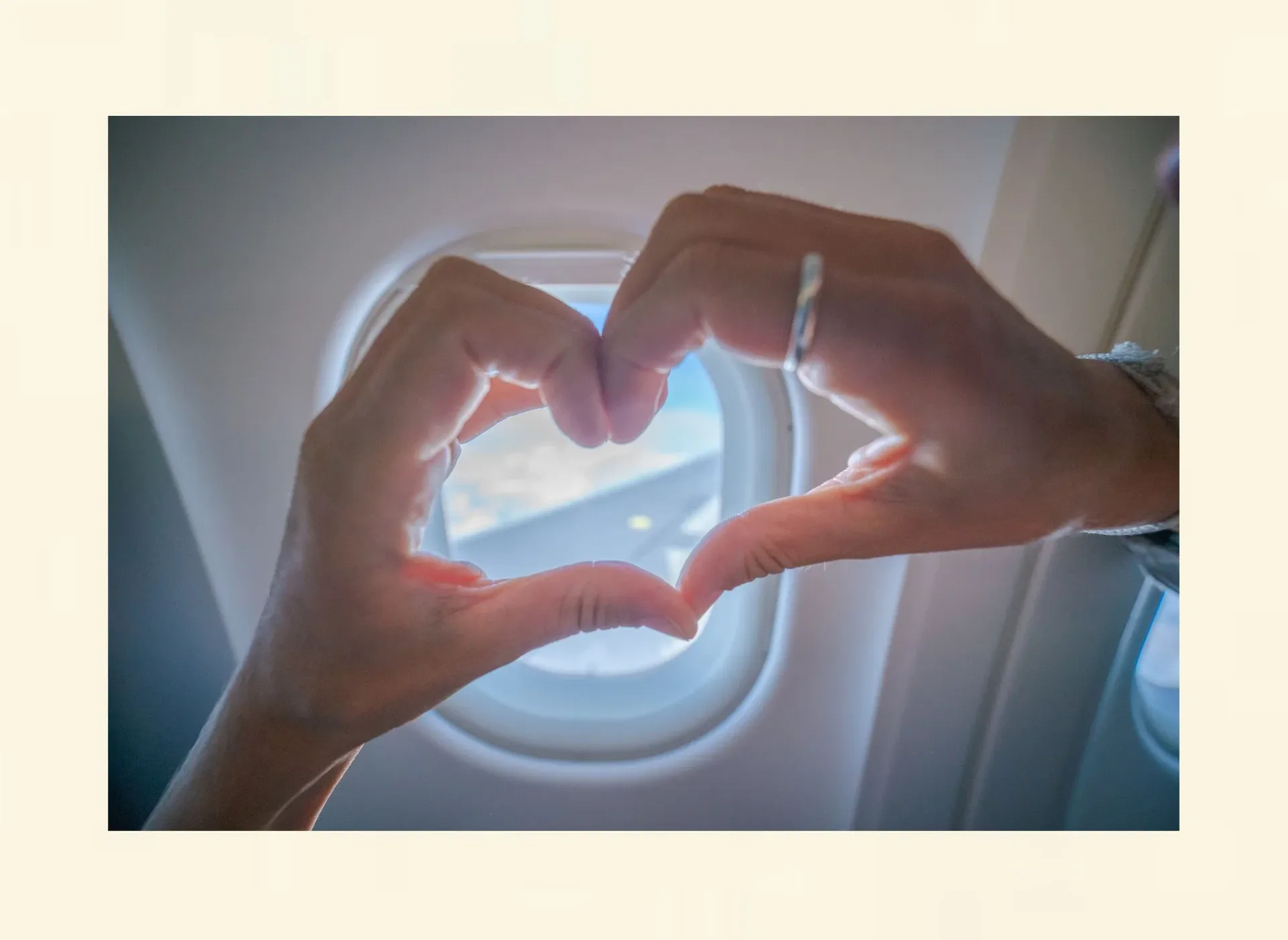 Person formt ein Herz mit den Händen vor dem Flugzeugfenster – mehr Sicherheit und Vertrauen durch Hypnose bei Flugangst